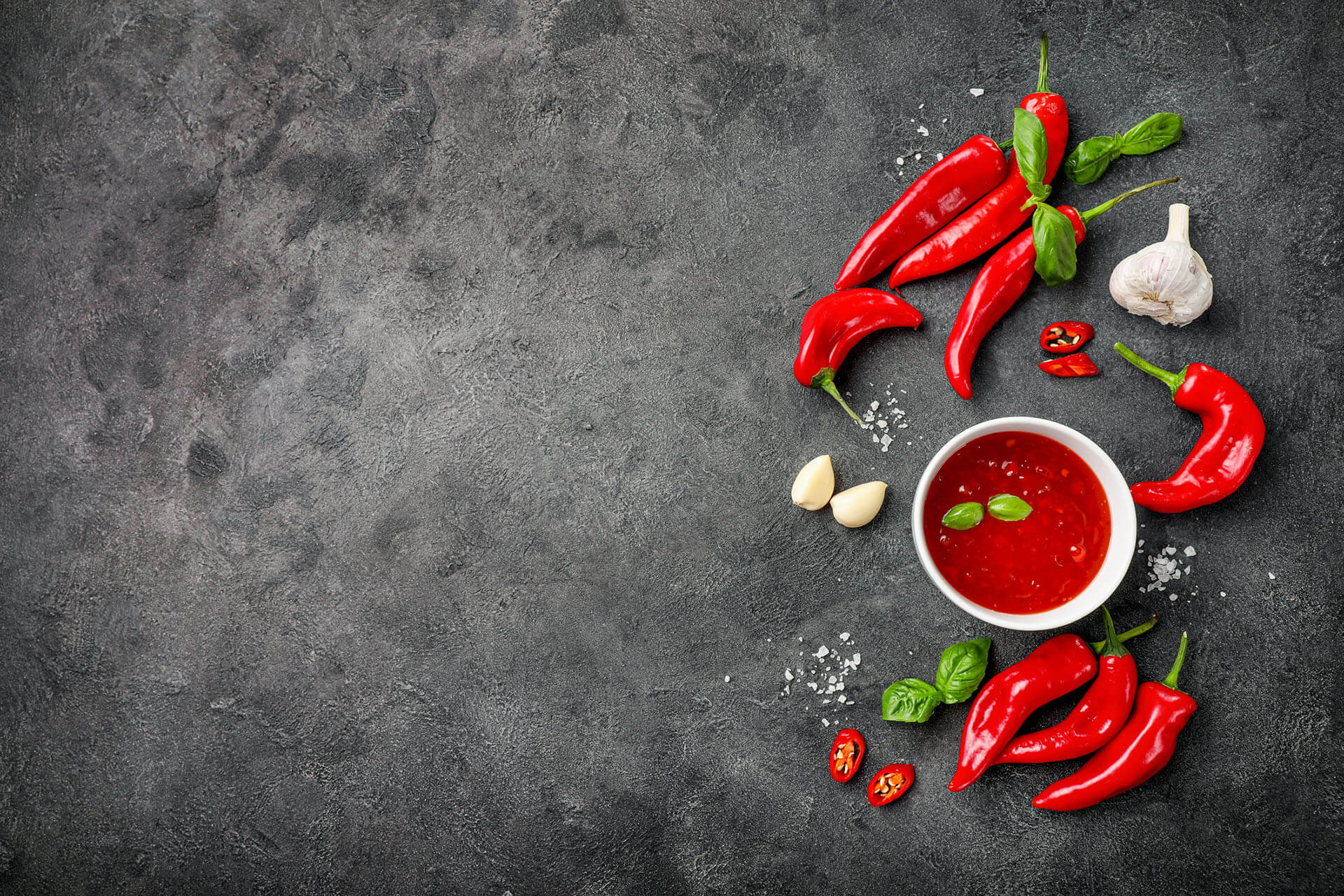 Hot spicy chili sauce in small bowl with chili red pepper and seasonings on black background. Top view. Copy space.